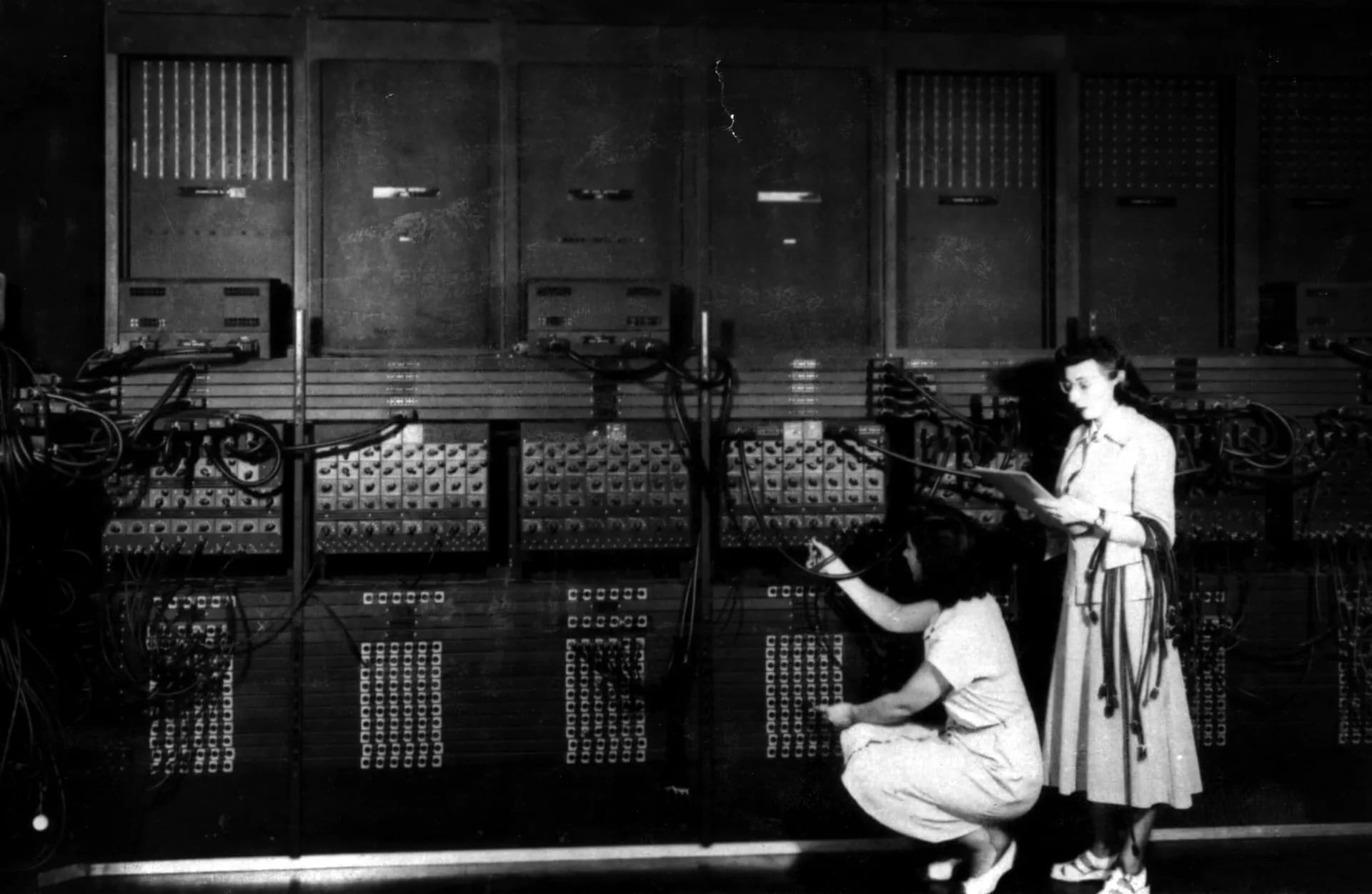 Two operators reprogramming the ENIAC, an early electronic computer, among its racks of cabling