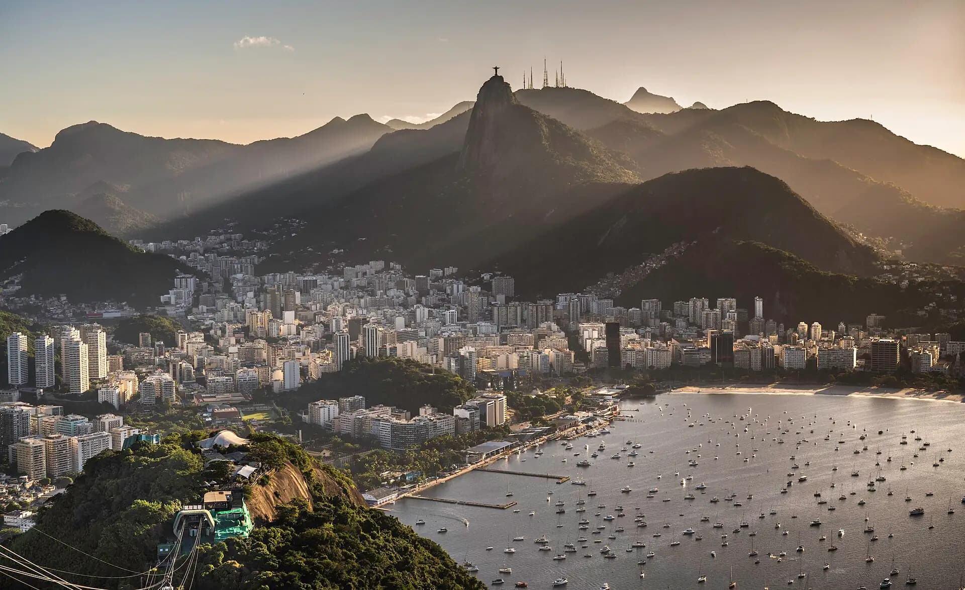 A city skyline at dusk along the water, towers against the hills behind it